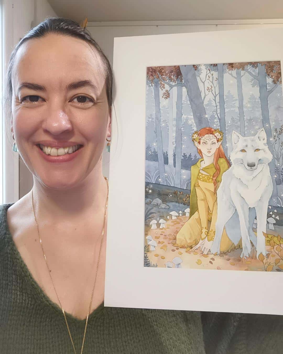 Portrait Aemarielle + aquarelle féerique Portrait de l'artiste Aemarielle tenant une de ses aquarelles près de son visage.